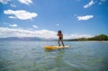 deska SUP Aqua Marina Fusion w ruchu na spokojnym morzu z górzystą linią brzegową w tle