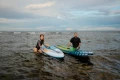 kobieta i mężczyzna z deskami SUP Gladiator wychodzą z morza na kamienistą plażę (2).webp