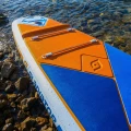 Gladiator Elite 12'6LT – rufa deski SUP na kamienistym brzegu, pomarańczowy deckpad i linki bagażowe