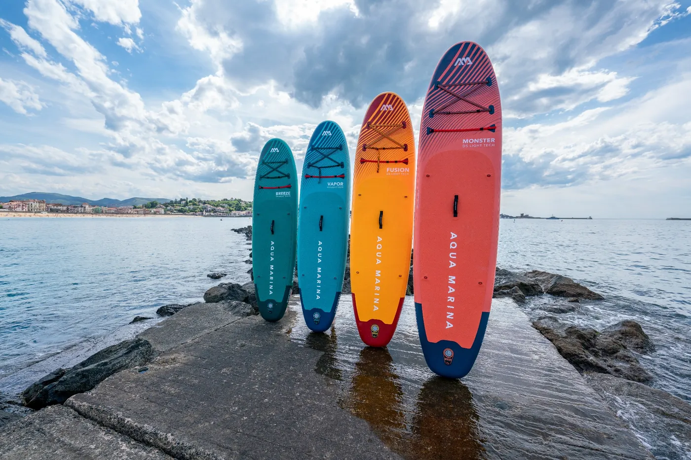 Cztery deski SUP Aqua Marina allround o różnych rozmiarach ustawione na nabrzeżu nad morzem – jak dobrać deskę SUP do wagi użytkownika