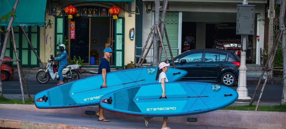 Para z deskami SUP Starboard Lite niesie lekkie, turkusowe deski ulicą w mieście – łatwy transport i mobilność deski SUP